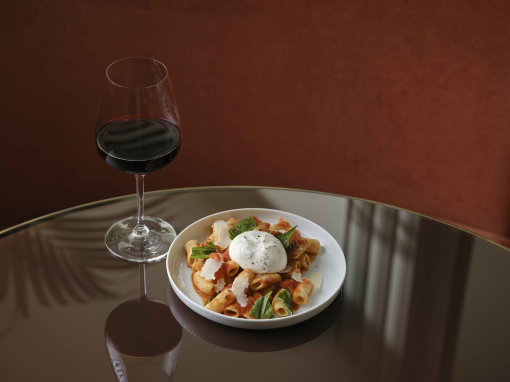A plate of pasta with sauce and cheese, paired with a glass of red wine.